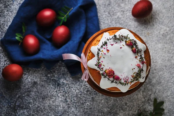 Paskalyayı kutlamak için ev yapımı kek ve kırmızı yumurta. Paskalya sembolleri. Kurumuş çiçeklerle süslenmiş Paskalya pastası, taze otlar, krema ve kurdele..