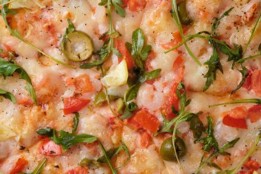 Pizza with tomatoes, shrimps, arugula, olives, lemon, mozzarella cheese, spices and tomato sauce. A closeup of a pizza.