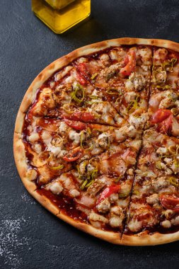 Pizza with tomato, chicken, ham, onion, sesame, mozzarella cheese, spices, tomato sauce and teriyaki sauce. On a dark background.