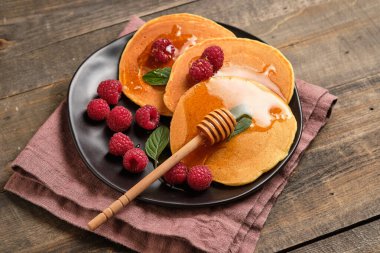 Flavored pancakes with honey and fresh raspberries for breakfast. Great breakfast dessert, garnished with fresh mint leaves.