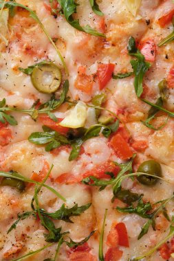 Pizza with tomatoes, shrimps, arugula, olives, lemon, mozzarella cheese, spices and tomato sauce. A closeup of a pizza.
