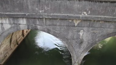 Çok eski bir taş köprü kemerin hemen altında ve köprünün altında nehirden akan bir su var.