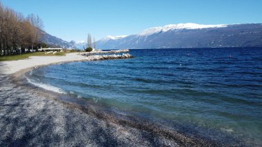 Toscolano Maderno 'daki çakıl taşı plajı. Karlı dağları ve Garda Gölü, İtalya.
