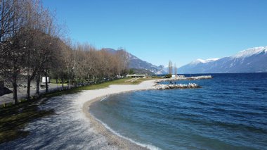 Toscolano Maderno 'daki çakıl taşı plajı. Karlı dağları ve Garda Gölü, İtalya.