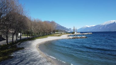 Toscolano Maderno 'daki çakıl taşı plajı. Karlı dağları ve Garda Gölü, İtalya.