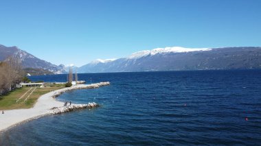 Toscolano Maderno 'daki çakıl taşı plajı. Karlı dağları ve Garda Gölü, İtalya.