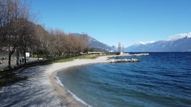 Toscolano Maderno 'daki çakıl taşı plajı. Karlı dağları ve Garda Gölü, İtalya.
