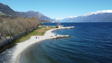 Toscolano Maderno 'daki çakıl taşı plajı. Karlı dağları ve Garda Gölü, İtalya.