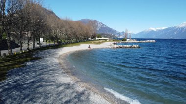 Toscolano Maderno 'daki çakıl taşı plajı. Karlı dağları ve Garda Gölü, İtalya.