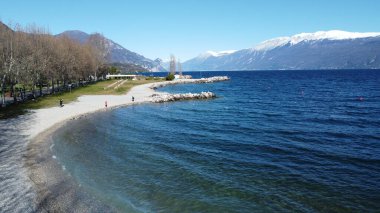 Toscolano Maderno 'daki çakıl taşı plajı. Karlı dağları ve Garda Gölü, İtalya.