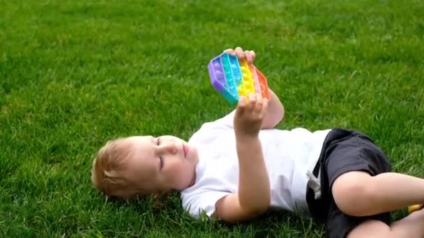 Ребенок играет с поп-сенсорной игрушкой. Мальчик нажимает на красочные радужные мягкие силиконовые пузыри. Традиционная фитнес-игра для детей и взрослых. образовательная игрушка. Simple Dimple — стоковое видео
