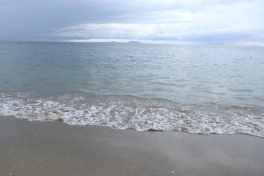 Sahildeki dalgalar kıyıya vurdu ve bulutlu gökyüzü.
