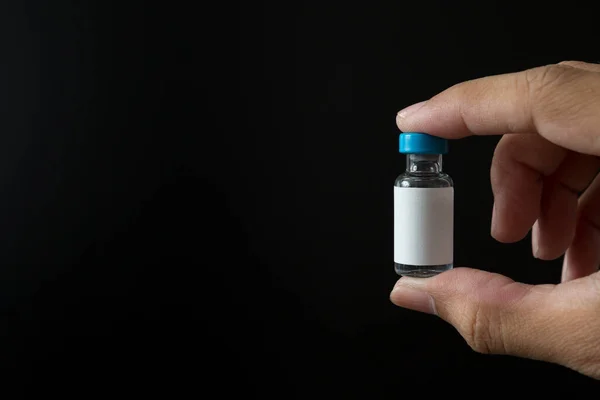 Hand holding vaccine bottles on black background for the Covid 19 concept and copy space