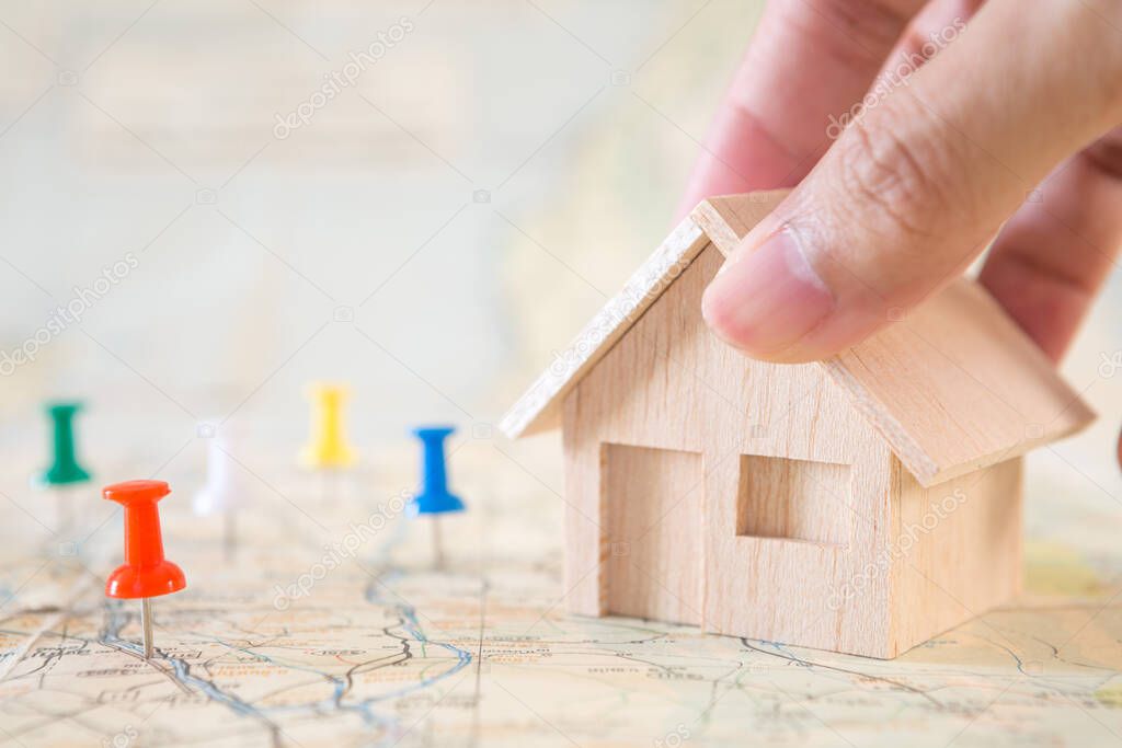 Selective focus of red pin and hand holding house model on map background for real estate concept