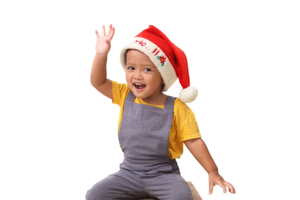 Sevimli Asyalı küçük kız Noel Baba 'nın şapkasını takmış oturuyor. Noel çocukları konsepti. Beyaz arkaplanda izole