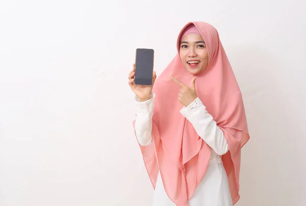 ピンクのベールやヒジャーブを身に着けている幸せなアジアのイスラム教徒の女性の肖像画や白いドレスを見せ 空白のスマートフォンの画面を指しています コピースペース付きの白い背景 — ストック写真