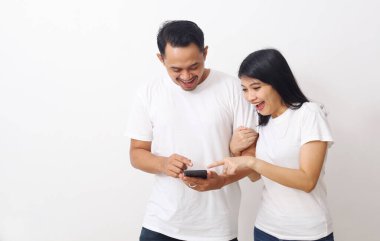 Mutlu Asyalı çift akıllı telefonlarına bakıp işaret ederken şaşırdı. Akıllı telefondan iyi haber al. Kopyalama alanı ile beyaza izole edilmiş