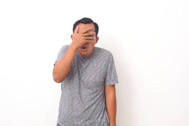 Korkak Asyalı adamın portresi, beyaz arka planda tek başına duran, elleriyle yüzünü kapatıyor. İnsan duyguları, yüz ifadesi konsepti. Ön görünüm