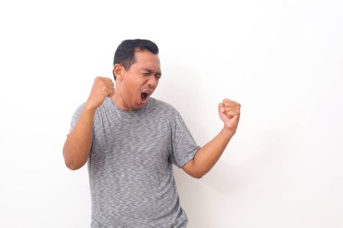 Mutlu galip. Genç, yakışıklı Asyalı adam beyaz arka planda dururken el kol hareketi yapıyor ve ağzını açık tutuyor.