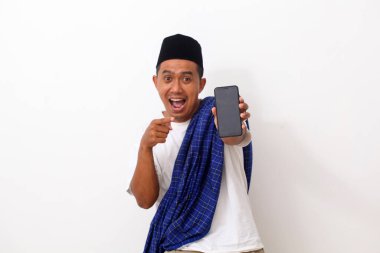 Asyalı mutlu bir adamın portresi, ayakta dururken, tutarken ve cep telefonuna işaret ederken. Beyazda izole edilmiş. Ramazan kavramı