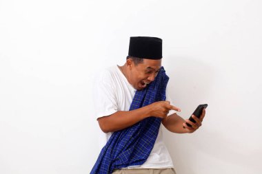 Asyalı mutlu bir adamın portresi, ayakta dururken, tutarken ve cep telefonuna işaret ederken. Beyazda izole edilmiş. Ramazan kavramı