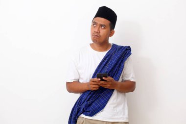 Asyalı düşünceli bir adam cep telefonunu tutarken ve boş bir alana bakarken. Beyaz arkaplanda izole