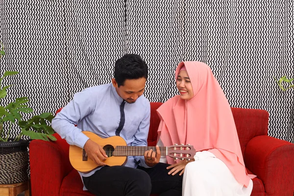 Pasangan Muslim Asia Duduk Sofa Merah Saat Bermain Gitar — Stok Foto