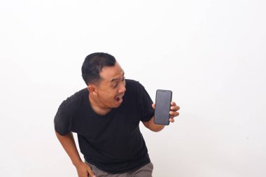 Siyah tişörtlü, cep telefonunu gösteren ve kameraya gülümseyen, cihaz veya mobil uygulama öneren tatmin olmuş Asyalı bir adamın portresi. Beyaz arka planda izole edilmiş kapalı stüdyo çekimi
