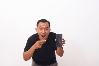 Siyah tişörtlü, cep telefonunu gösteren ve kameraya gülümseyen, cihaz veya mobil uygulama öneren tatmin olmuş Asyalı bir adamın portresi. Beyaz arka planda izole edilmiş kapalı stüdyo çekimi