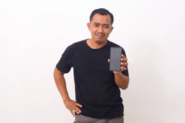 Siyah tişörtlü, sakallı, cep telefonuna gülümseyen, cihaz ya da mobil uygulama öneren Asyalı adamın portresi. Beyaz arka planda izole edilmiş kapalı stüdyo çekimi