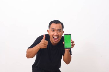 Siyah tişörtlü, cep telefonunu gösteren ve kameraya gülümseyen, cihaz veya mobil uygulama öneren tatmin olmuş Asyalı bir adamın portresi. Beyaz arka planda izole edilmiş kapalı stüdyo çekimi