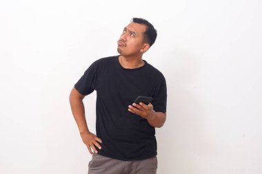 Asyalı bir adam yan bakarken ve cep telefonu tutarken bir şeyler düşünüyor. Kopyalama alanı ile beyaz arkaplanda izole