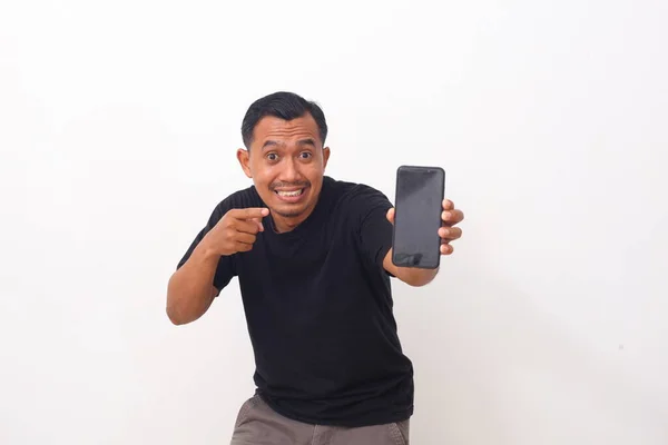 一个满意的亚洲男人的画像 他身穿黑色T恤 留着胡子 指着手机 对着相机微笑 推荐使用小工具或移动应用程序 在白色背景下隔离的室内拍摄 — 图库照片