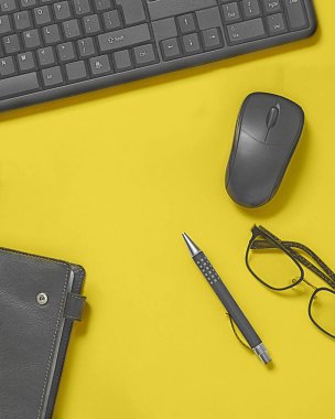Klavyeli parlak ofis masası, fare maketi, gözlük, deri kapaklı defter, kalem. Kopyalama alanı olan dikey üst görünüm. Sarı ve gri renkli 2021 renkleri. Merkez ofis en az çalışma alanı
