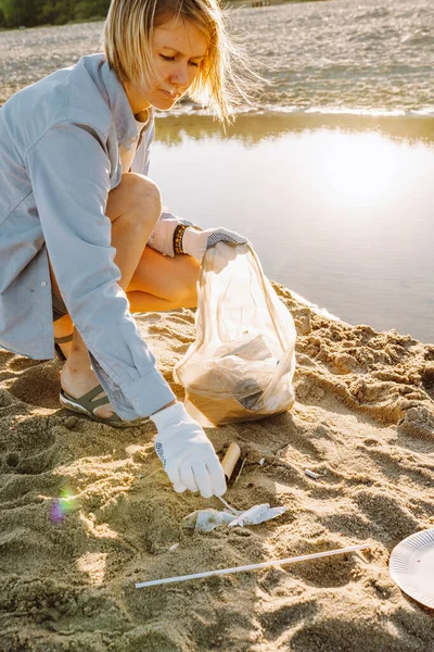Woman collect plastic garbage on sandy beach of the sea. Spilled garbage on the beach. Environmental pollution concept