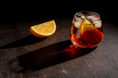 Koyu arkaplanda gölgesi olan prange dilimli Negroni kokteyli.