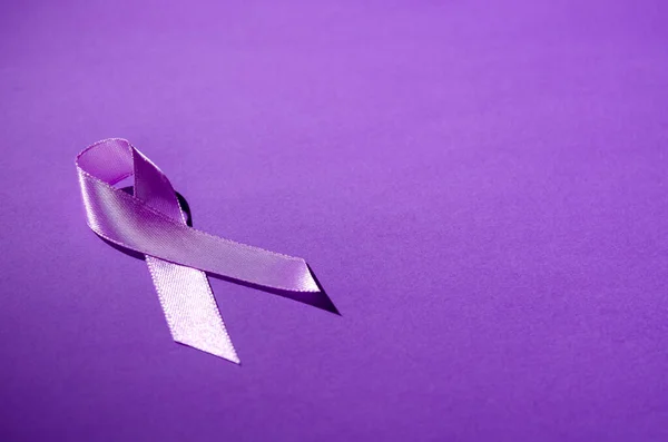 Purple awareness ribbon on a purple background. Copy space. World epilepsy awareness month.