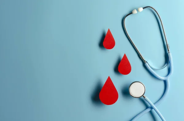 Símbolo de gota de sangre con estetoscopio sobre fondo azul. Día de la hemofilia, día del donante de sangre. Concepto — Foto de Stock