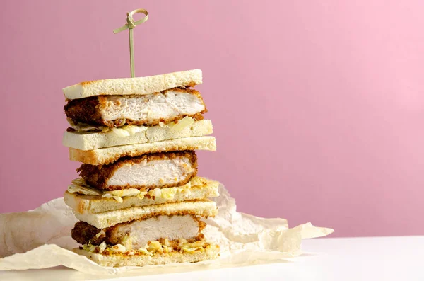 Katsu sandos japanese sandwich with chicken or pork chop, cabbage and tonkatsu sauce isolated on pink background.