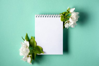 Turkuaz arka planda bahar çiçekli dalları olan boş bir defter. Düz yatıyordu. Üst görünüm.