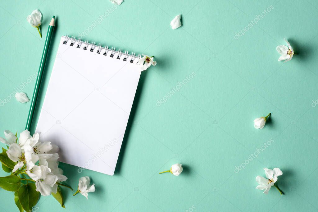 Empty notebook with spring flowering branches on a turquoise background. Flat lay. Top view.