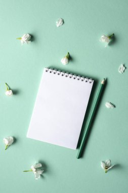 Turkuaz arka planda bahar çiçekli dalları olan boş bir defter. Düz yatıyordu.