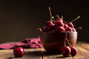 Tahta masadaki kirazlar ve kasede su damlaları.