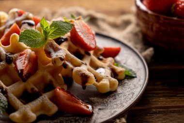 Çilekli waffle, çikolata soslu ve ahşap masada pudra şekerli.