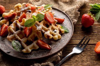 Çilekli waffle, çikolata soslu ve ahşap masada pudra şekerli.