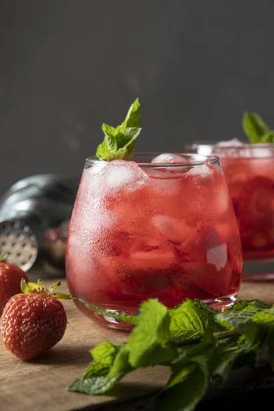 Boisson rouge avec fraise, glace et menthe. Cocktail d'été rafraîchissant dans un verre sur une table en bois — Photo