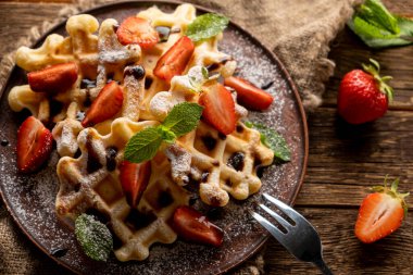 Çilekli waffle, çikolata soslu ve tahta üzerine pudra şekerli.