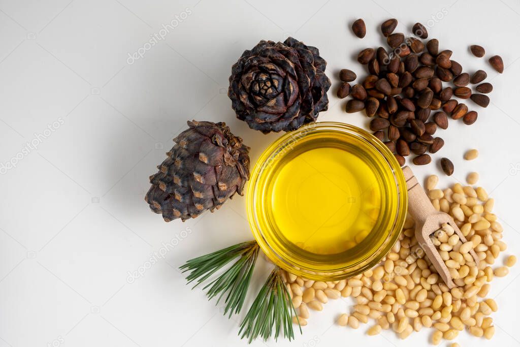 Pine nuts oil with peeled pine nuts and pine cones on white