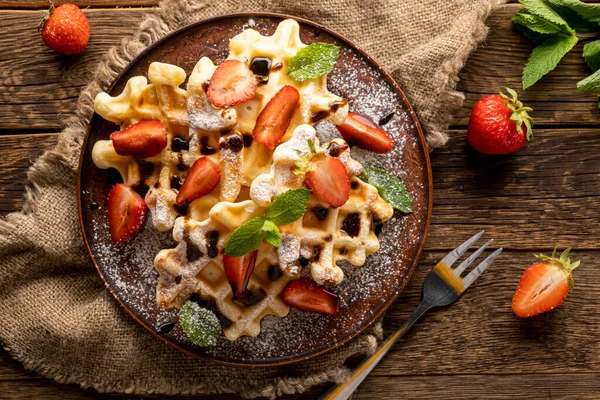 Gofres con fresas, cobertura de chocolate y azúcar en polvo en la mesa de madera — Foto de Stock