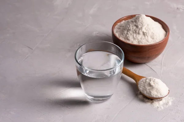 Polvo de colágeno con un vaso de agua sobre un fondo gris con espacio para copiar. —  Fotos de Stock